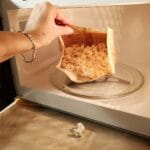 Hand touching opened bag of popcorn in microwave