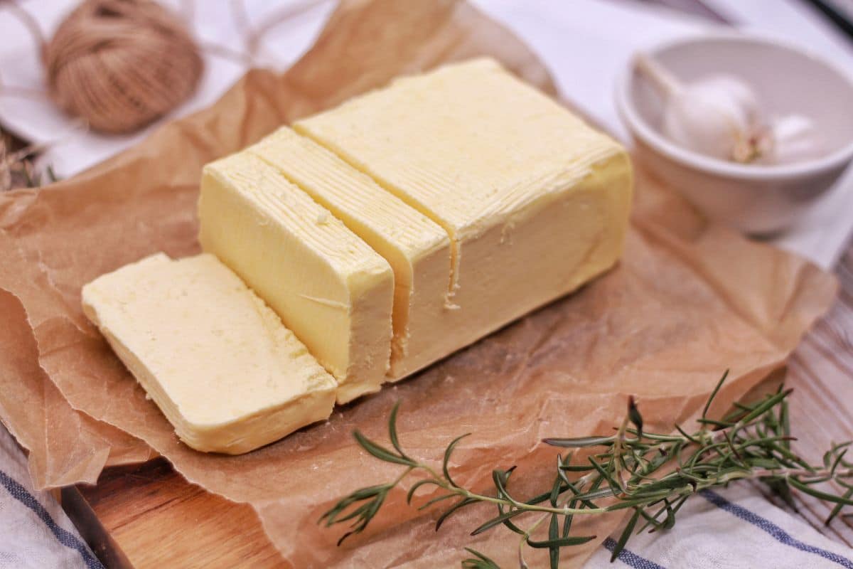 Block of butter partialy sliced on paper sheet with ingredients around