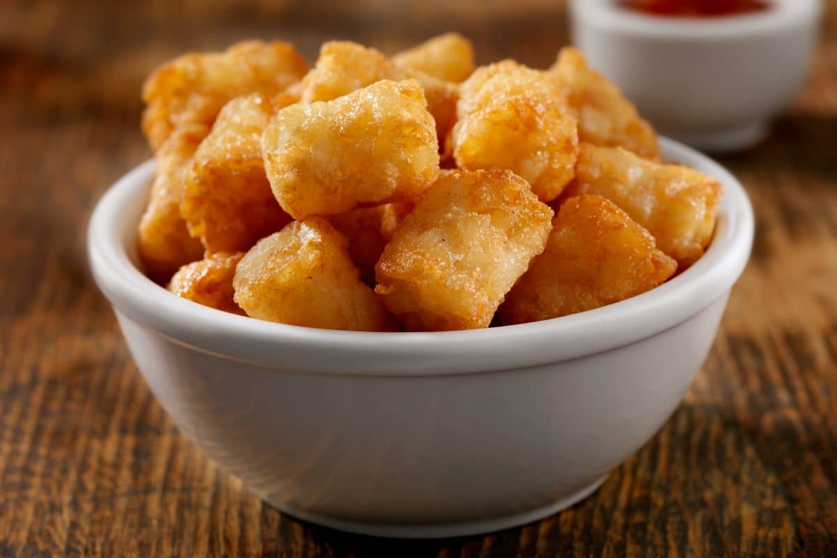 White bowl full of tater tots on wooden table