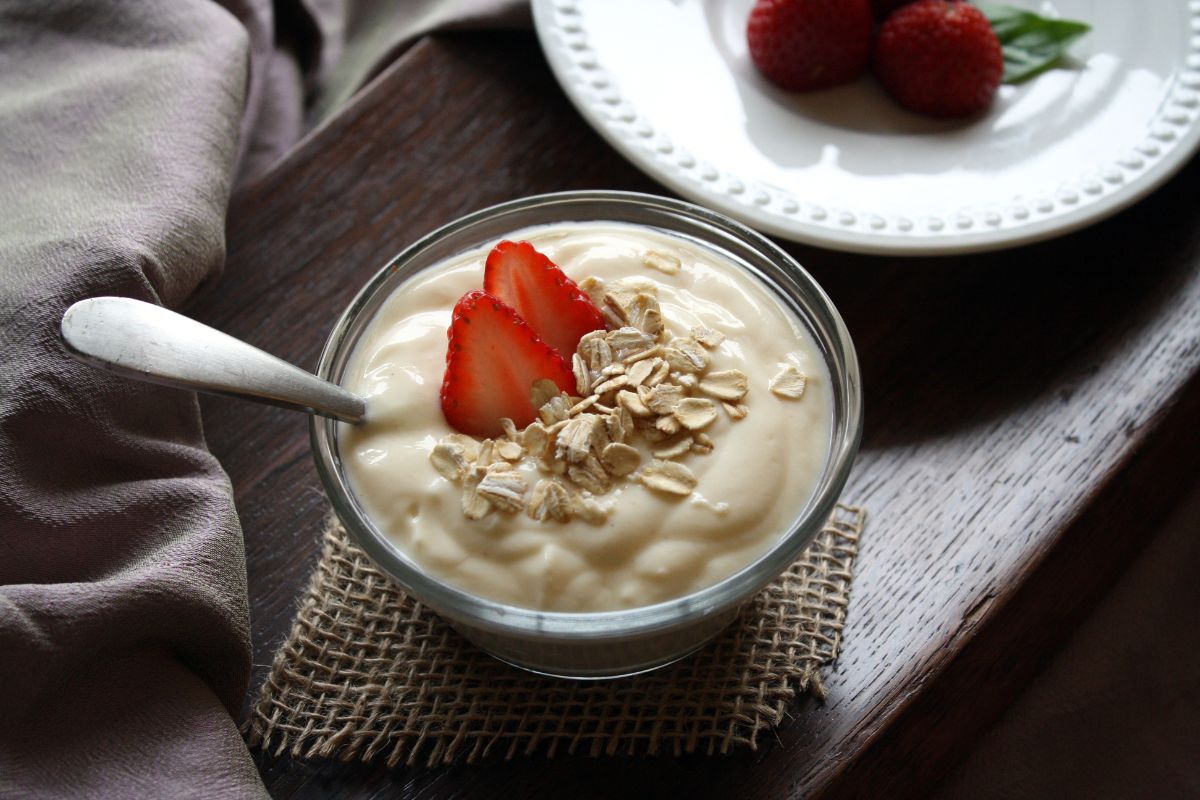 Bowl of yogurt with oat flakes, fruits and spoon on table