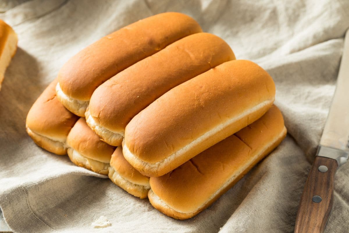 Bunch of hot dog buns on white table cloth with knife