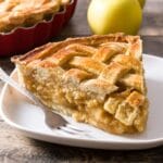 Slice of apple pie with fork on white plate