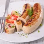 Two sausages with fork and sliced apple on white plate