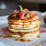 Pile of pancakes with dressing and fruits on white tray