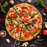 Sliced pizza with scattered ingredients around on black table