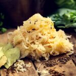 Fresh sauerkraut on wooden board with seasoning and ingredients around
