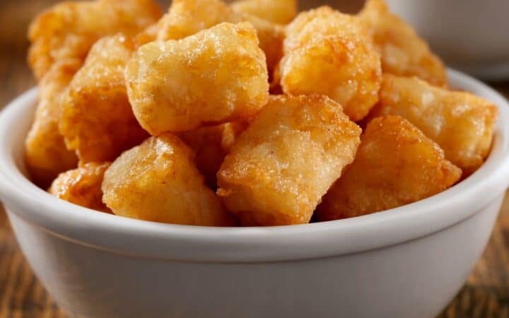 White bowl full of tater tots on wooden table