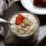 Bowl of yogurt with strawberries, oat flakes and spoon on table