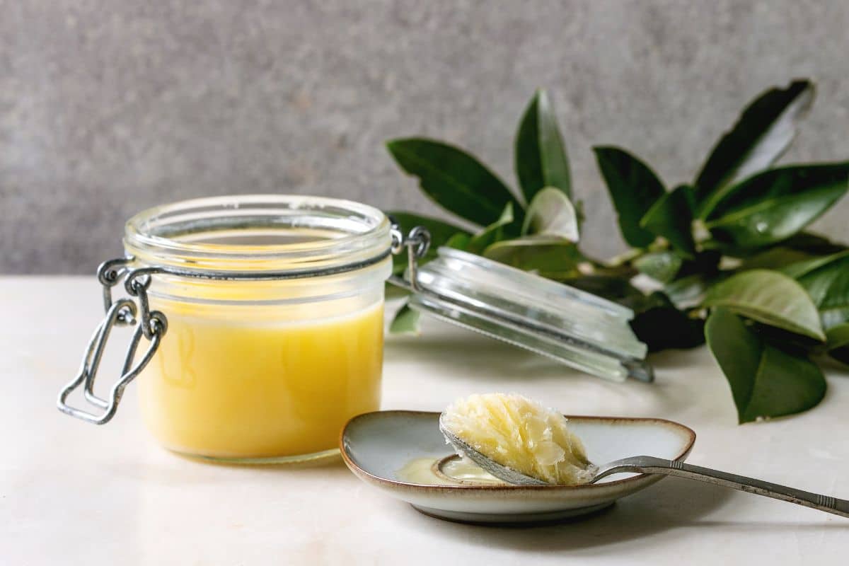 Clarified butter in glass jar and on spoon on plate  with herb on table