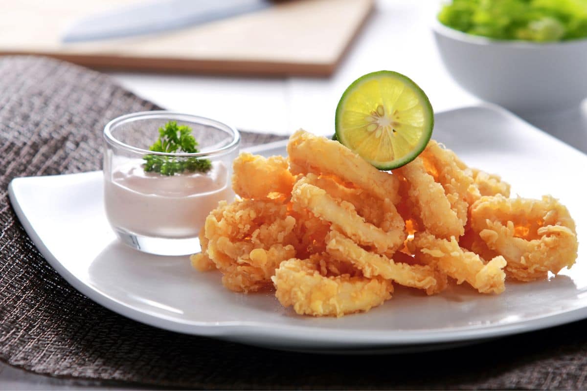 Fried calamari on white plate with dip and slice of lemon
