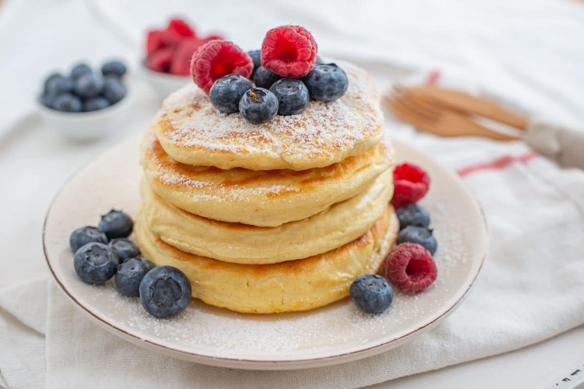 Pile of pancakes with raspberries and strawberies on white plate