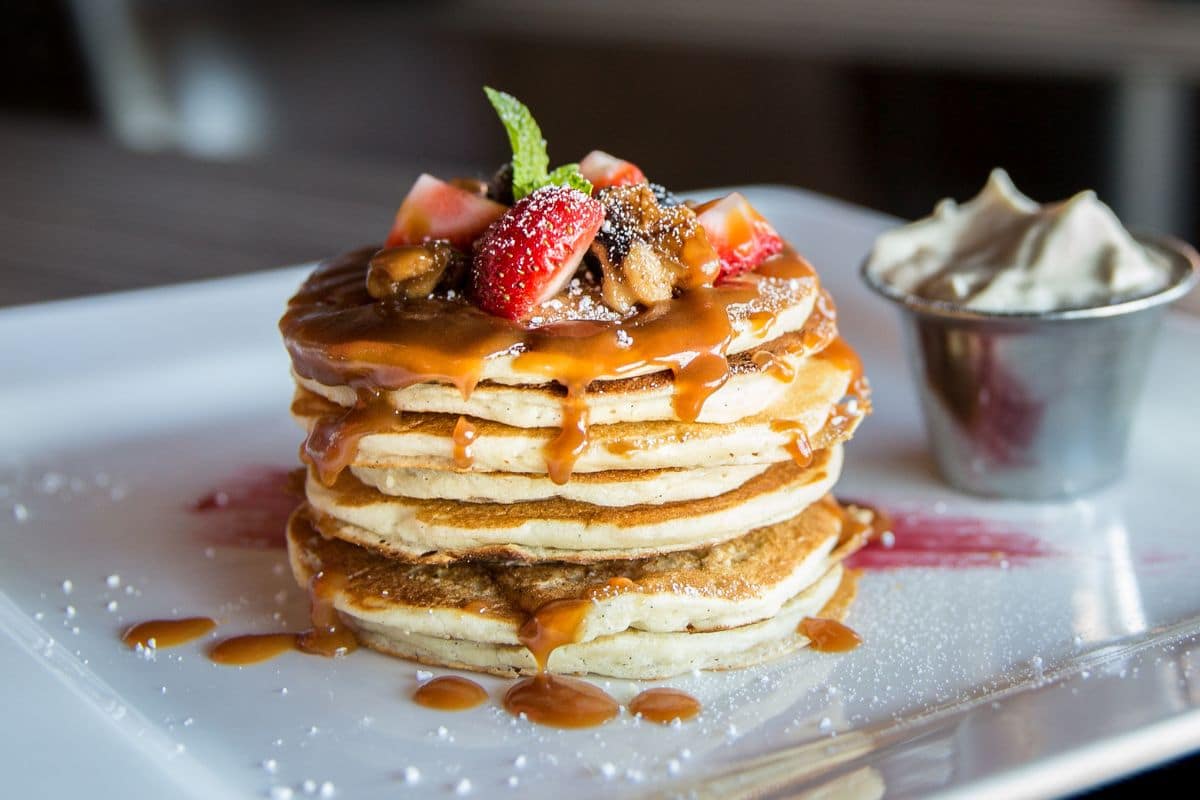 Pile of pancakes with fruits and dressing on white tray