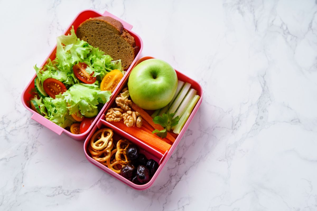 Pink lunch box full of fruits, vegetable, lunch dish on gray table