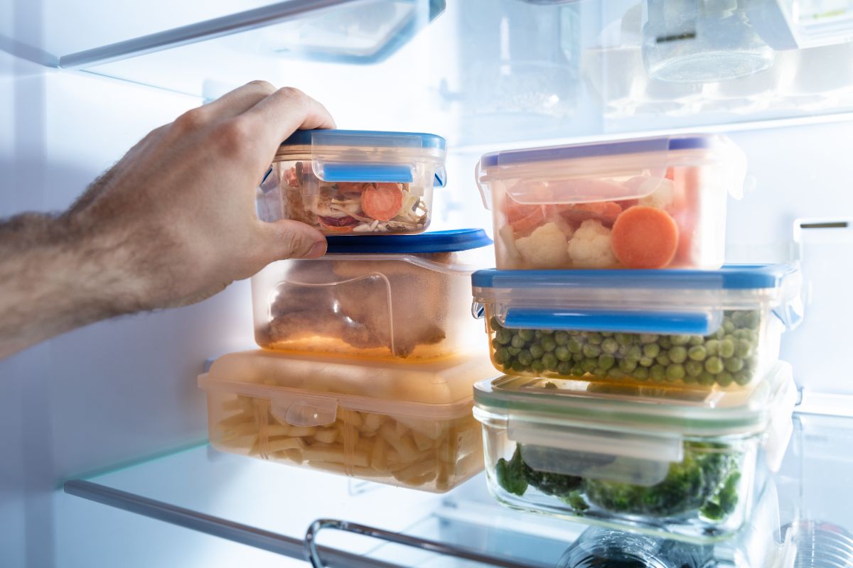 Hand touching plastic containers in refrigerator.