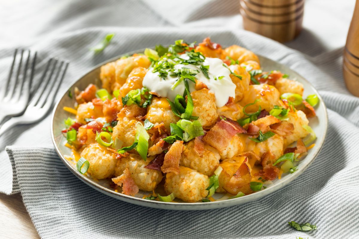 White plate full of tater tots with dip and vegetable on cloth wipe