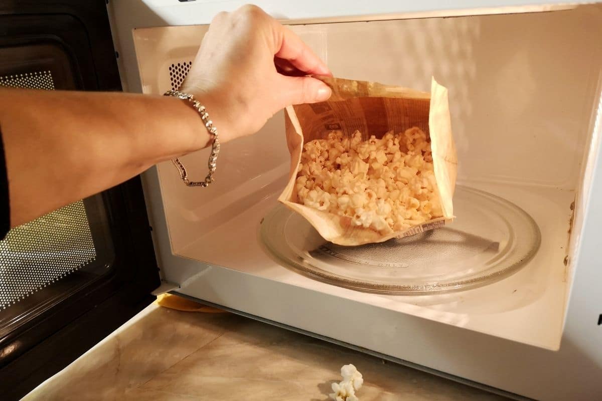 Hand touching opened bag of popcorn in microwave
