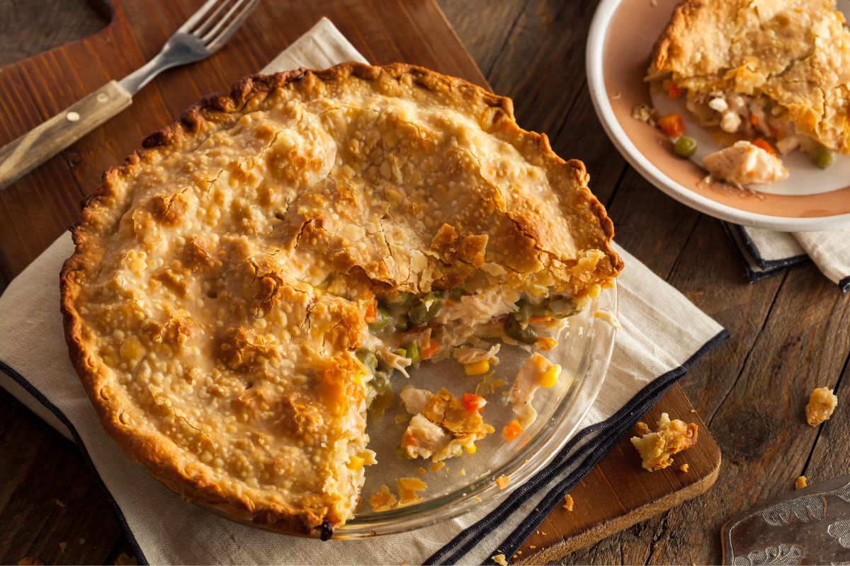 Pot pie on glass tray on on wooden board with fork and cloth wipe on table