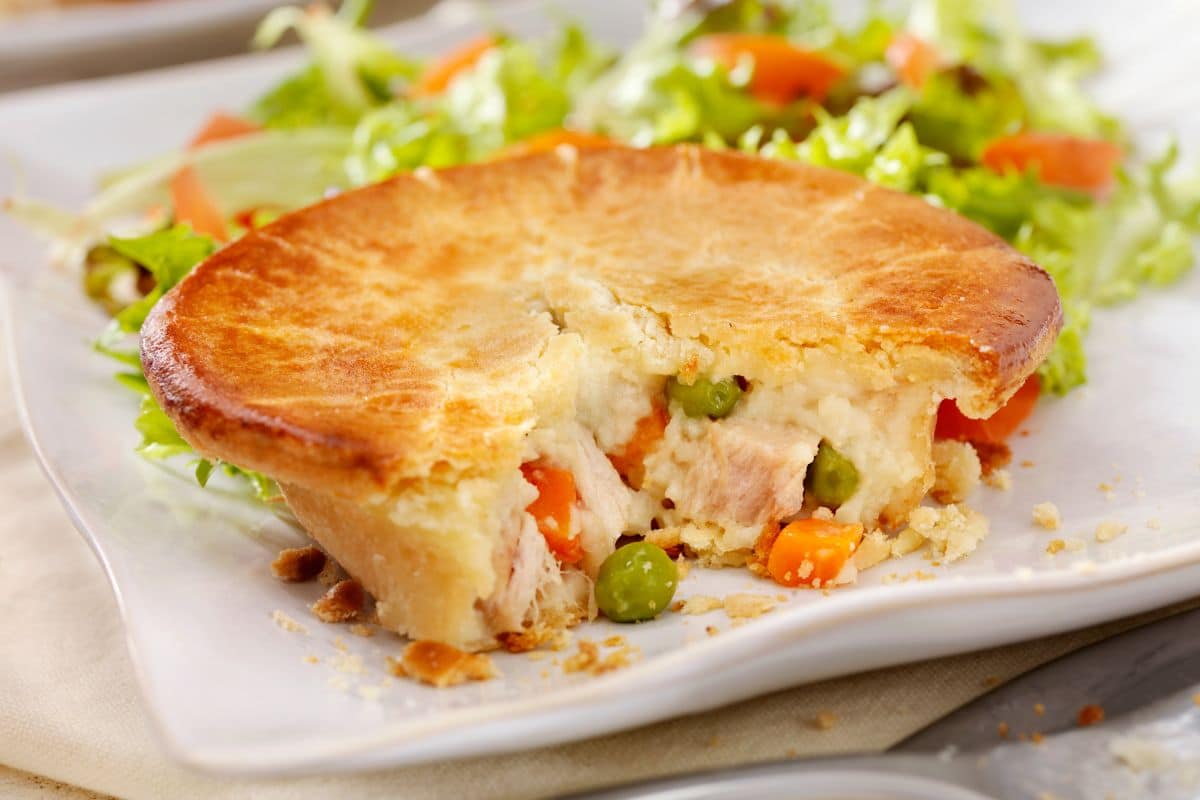 Partialy eaten pot pie on white plate with vegetable
