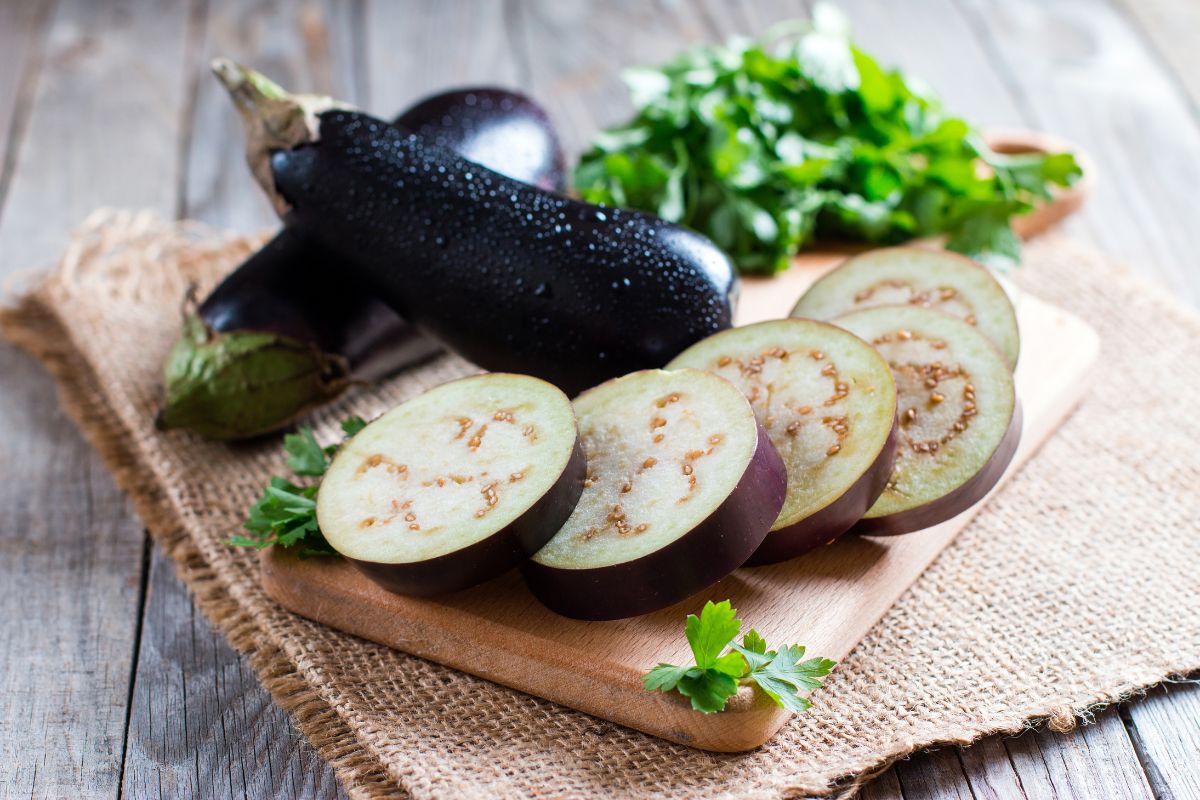 Sliced eggplant on wooden cutting board whole eggplants on table