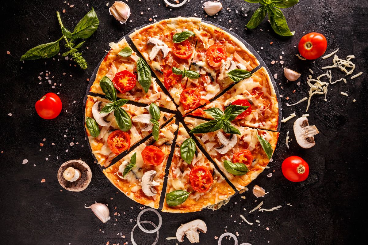 Sliced pizza with ingredients scattered on black table