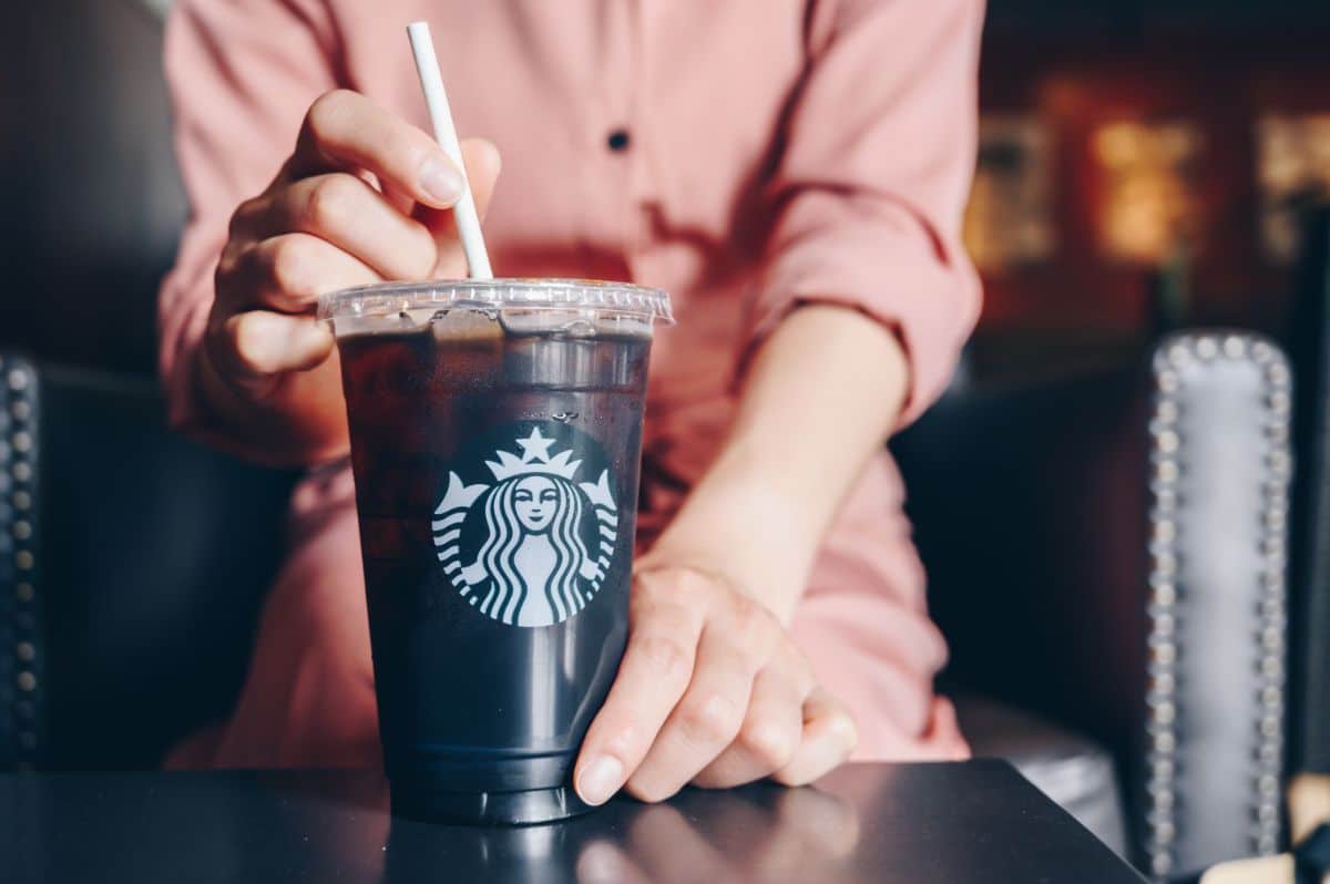 Hand touching starbucks iced coffe cup with straw on table