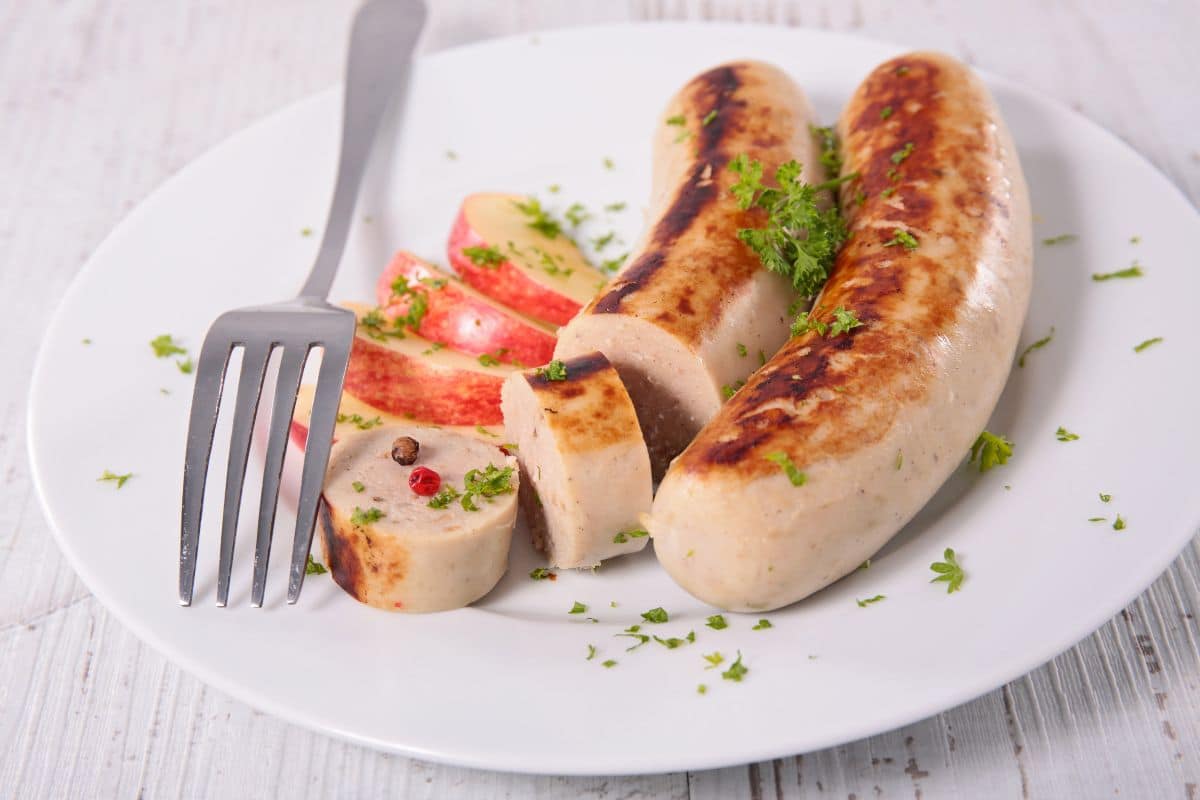 Two sausages with sliced apple and fork on white plate
