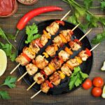 Kebab sticks on black pan with herbs,vegetables on wooden table