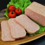 Spam lunch meat sliced on wooden board with tomatoes and salad