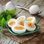 Sliced boiled eggs on plate on table with egg on spoon, eggs in mold and herbs