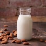 Glass jar of almond milk on table with scattered almonds around