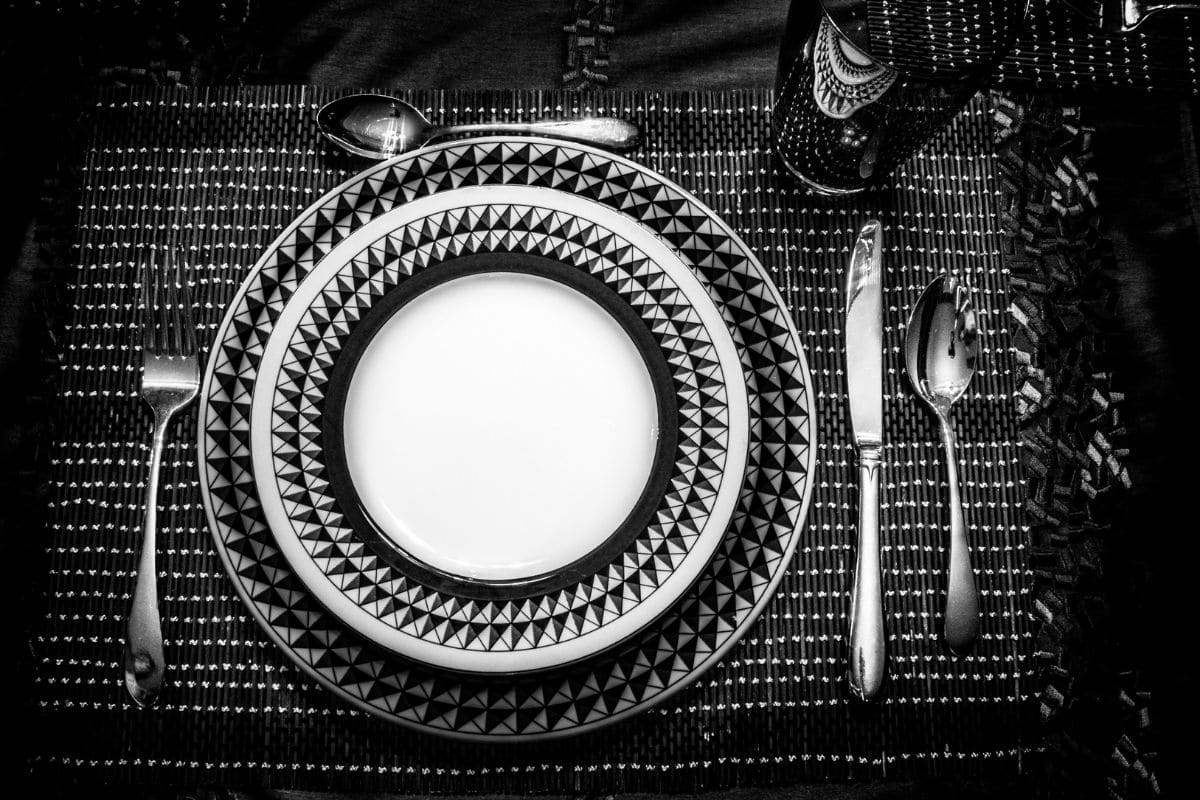 Black and white plates with spoon, knife, fork and glass cup on black-white pad