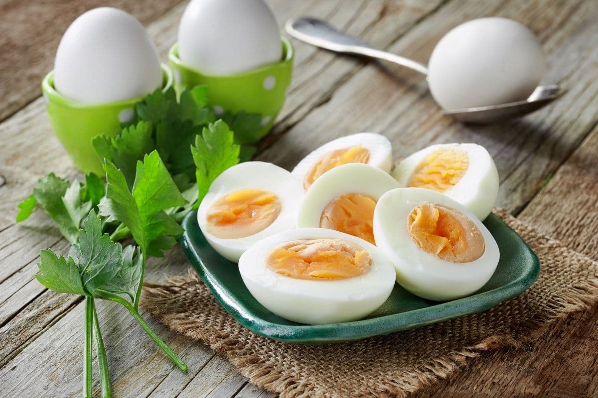 Sliced eggs on green plate with boiled eggs in molds, on spoon and wooden table with herbs