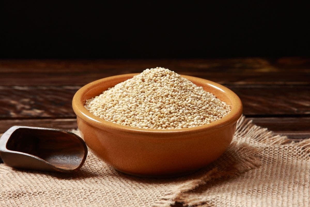 Brown bowl of quinoa on cloth pad with wooden spoon on wooden table