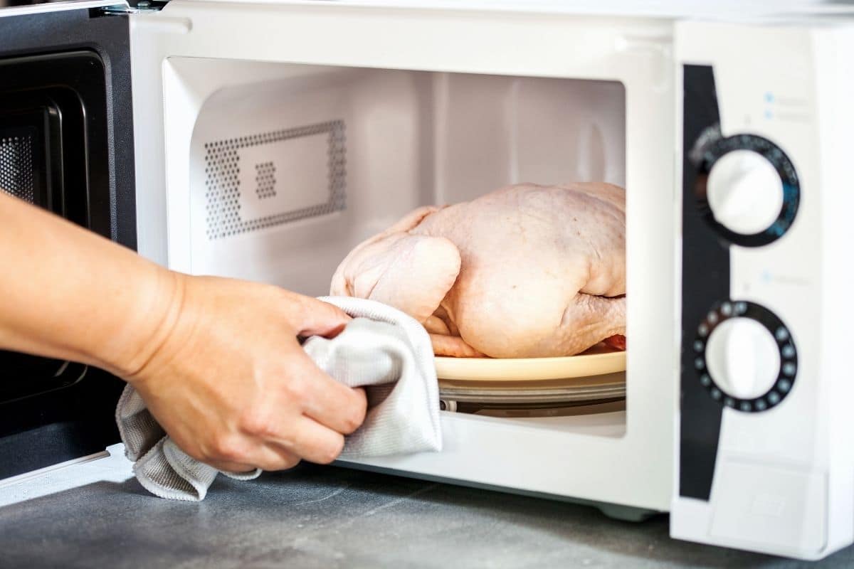 Hand holding whole chiken on plate in microwave by cloth wipe