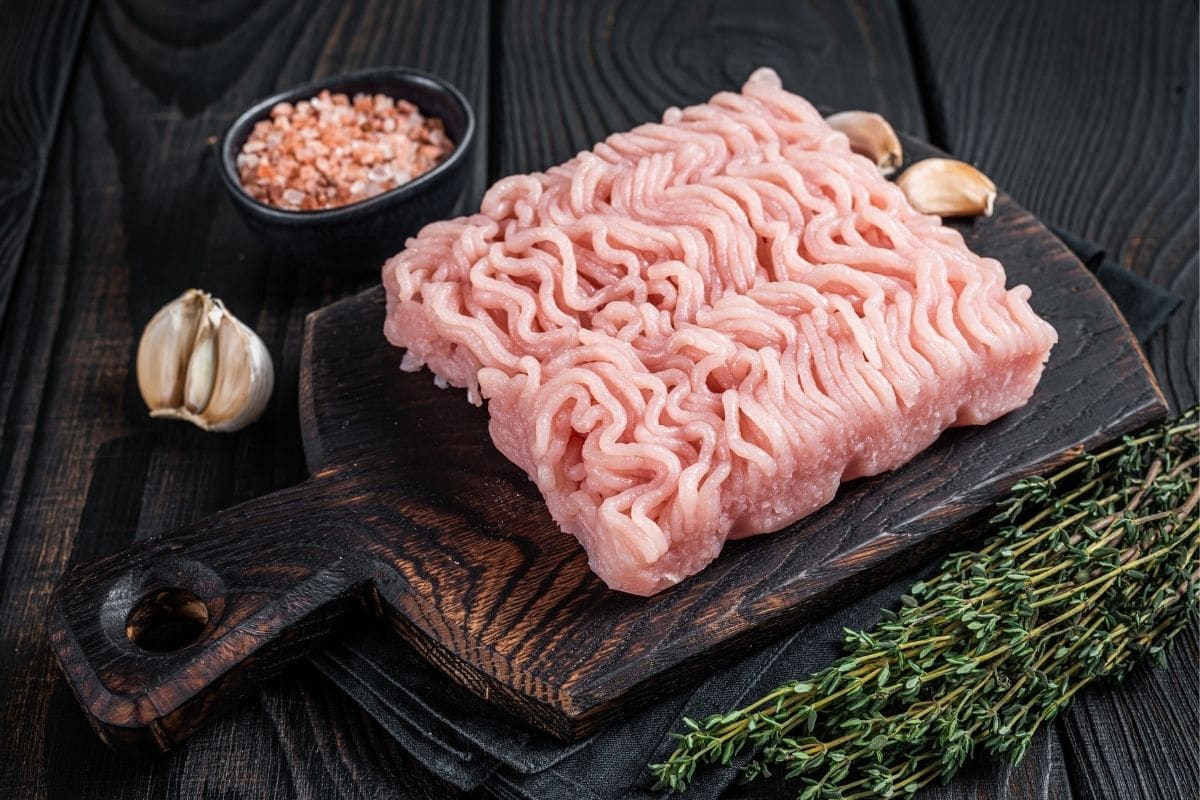 Ground turkey on wooden cutting board with herbs, garlic,bean on black table