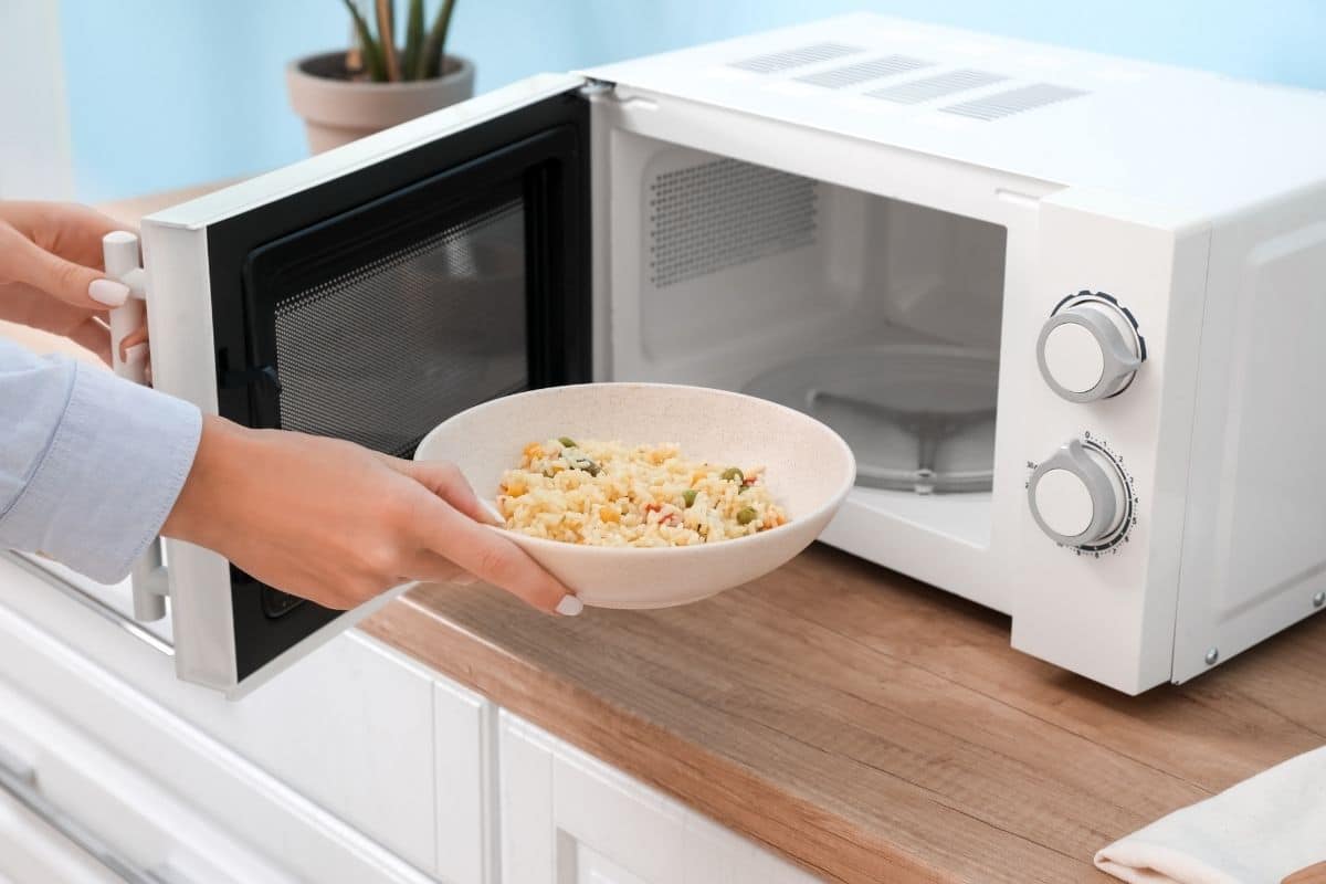 Woman holding bowl of rice infront of opened microwave