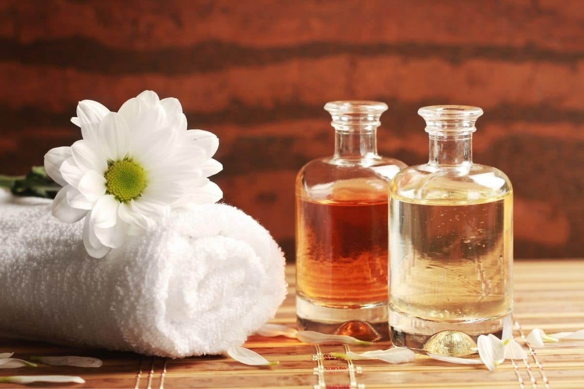 Glass bottle of massage oil with flower and towel on table