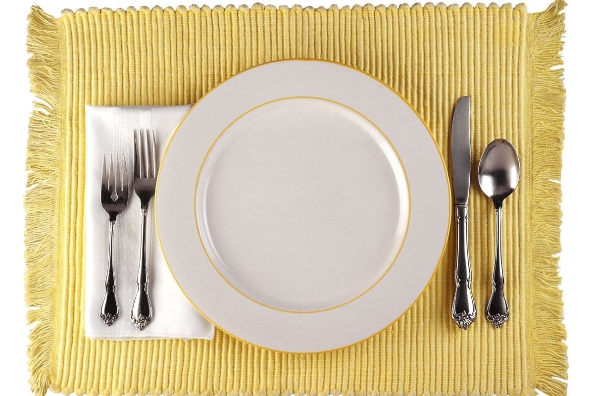 White plate with knife,spoon and forks on yellow pad