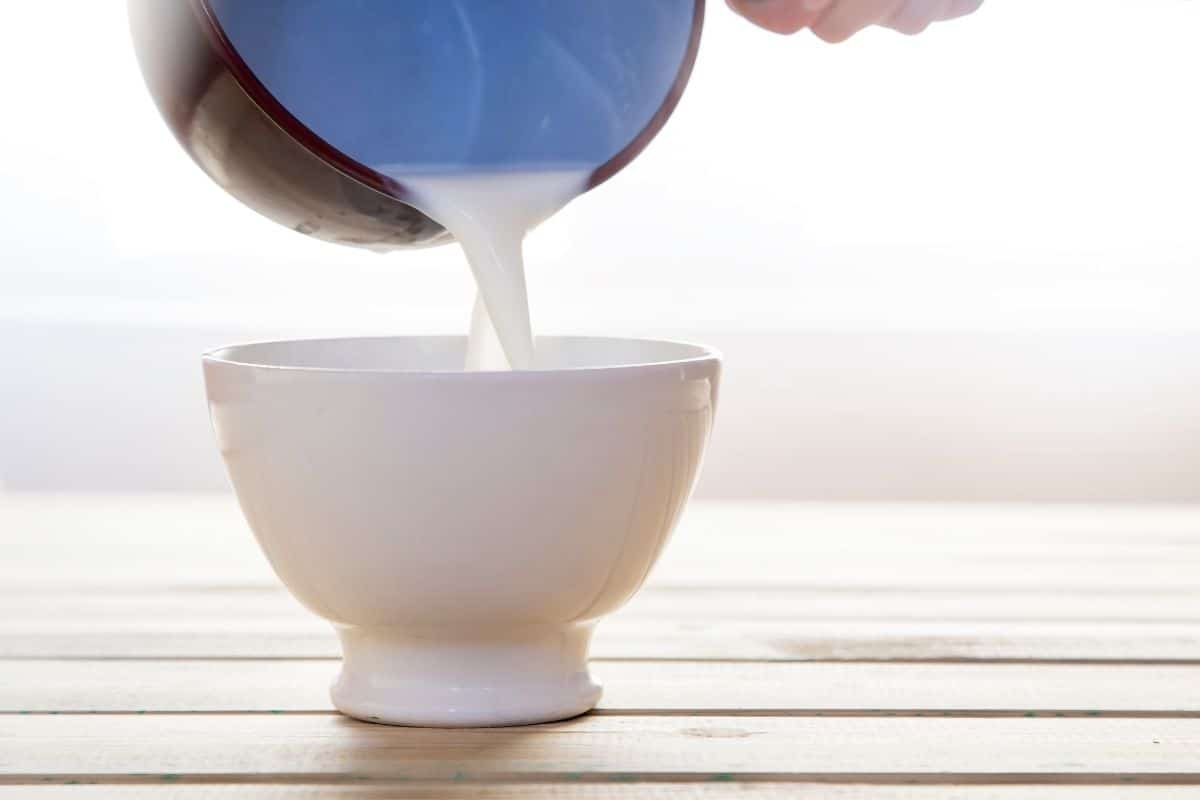 Milk from pot being poured into white bowl