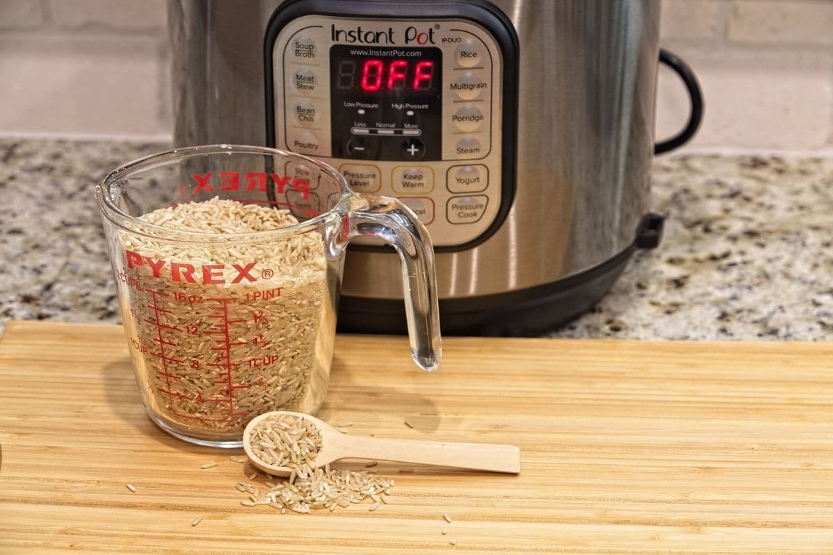Pyrex container with rice on wooden board and wooden spoon, instant pot cooker in the background