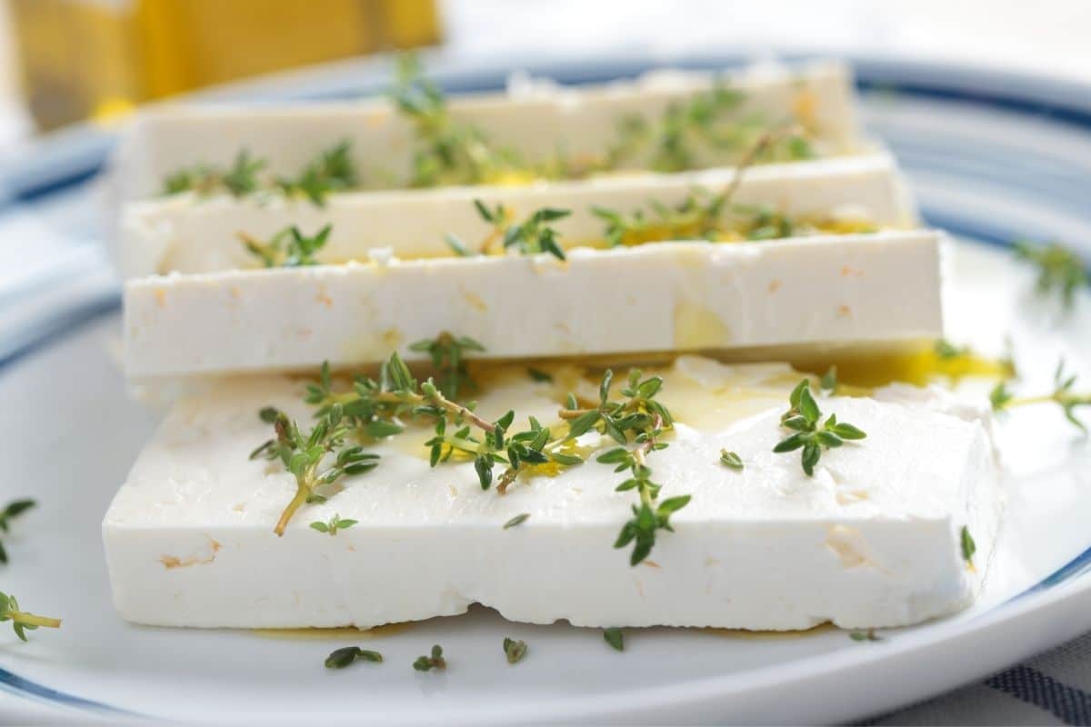 Sliced, seasoned feta cheese on blue-white plate with herbs