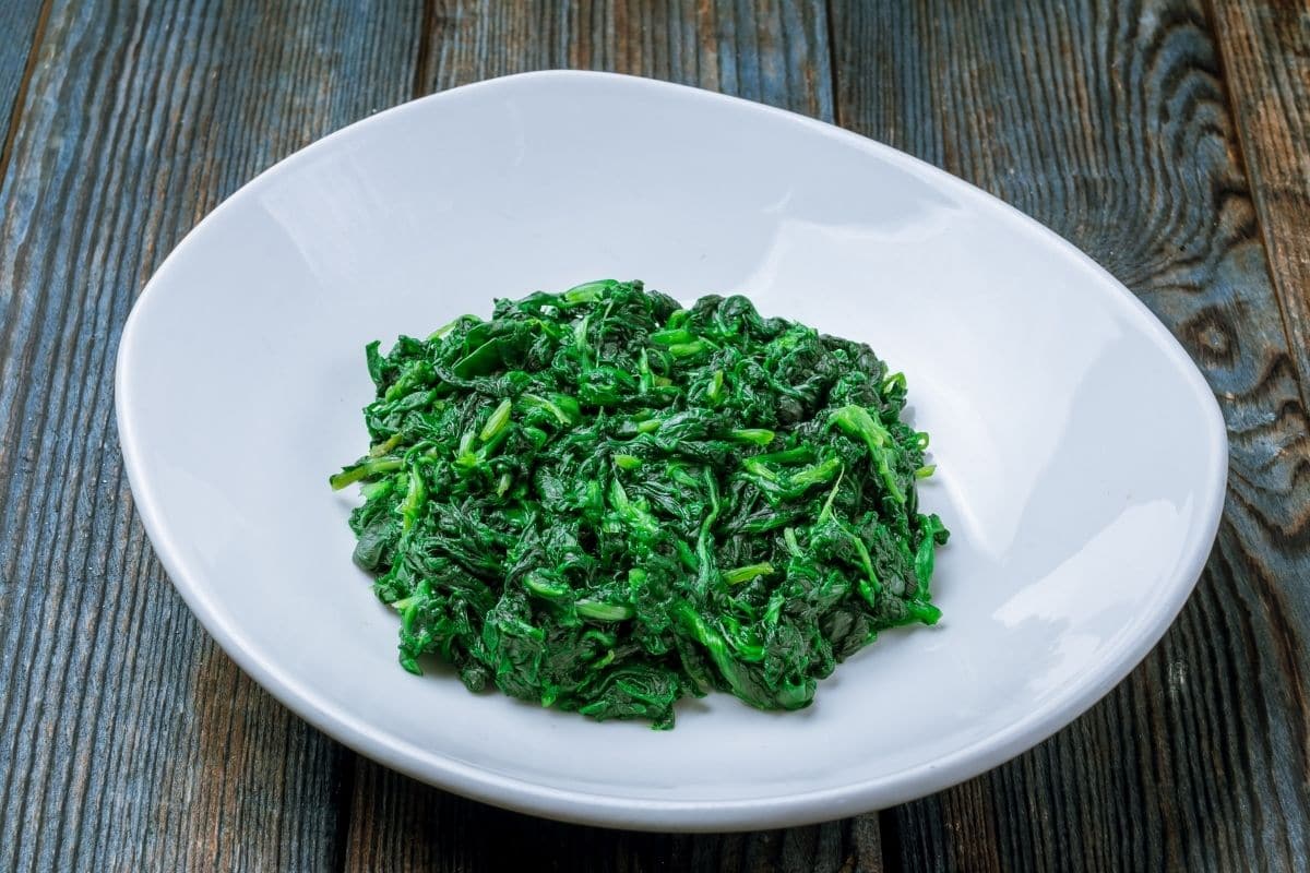 Steamed spinach on white plate on wooden table
