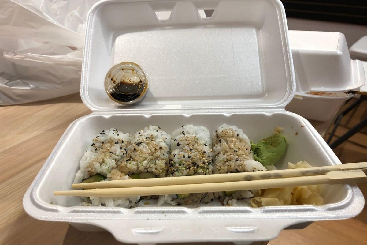 Sushi with wooden sticks and sauce in styrofoam container