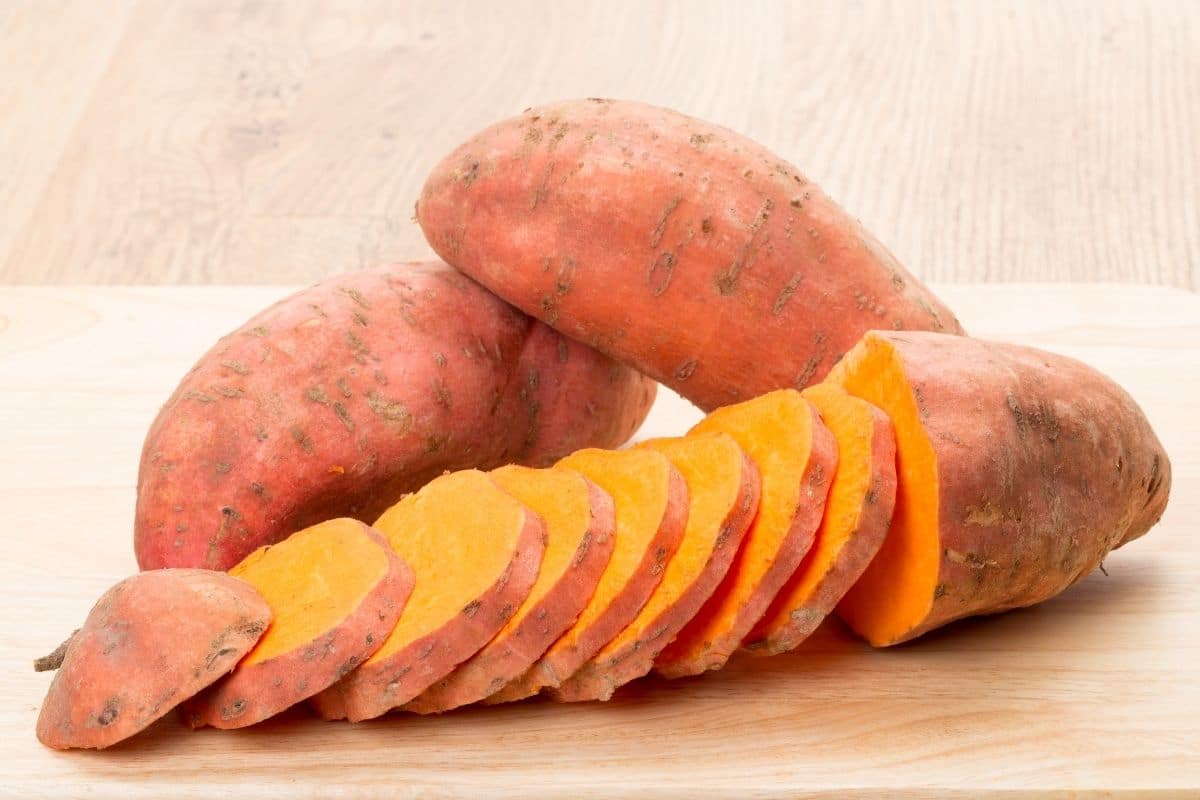 Two whole sweet potatoes and one sliced sweet potatoe on cuttin board