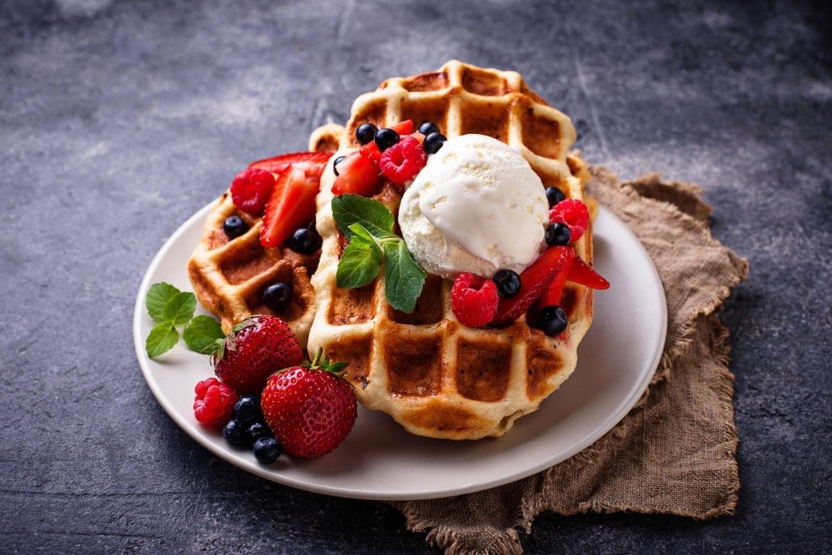 Waffles with whipped cream, herb, fruits on white plate on gray table