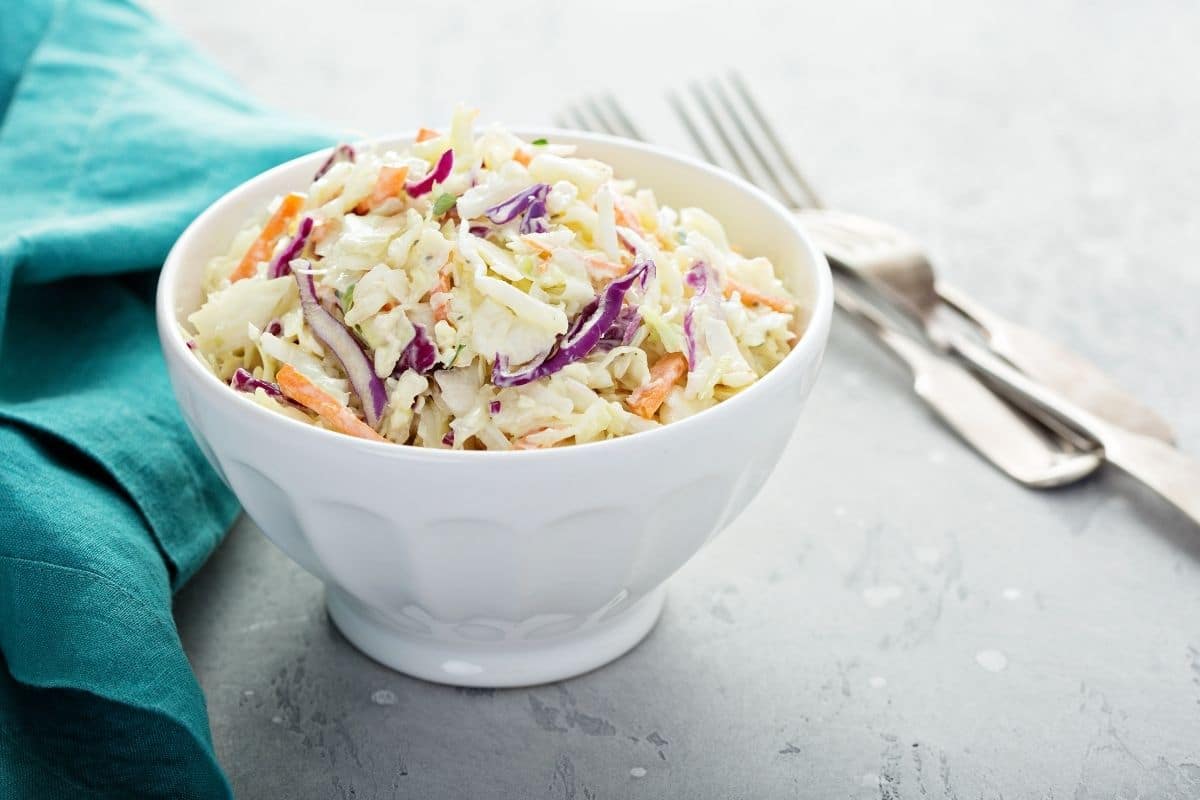 White bowl of coleslaw salad with forks and blue cloth wipe on gray table