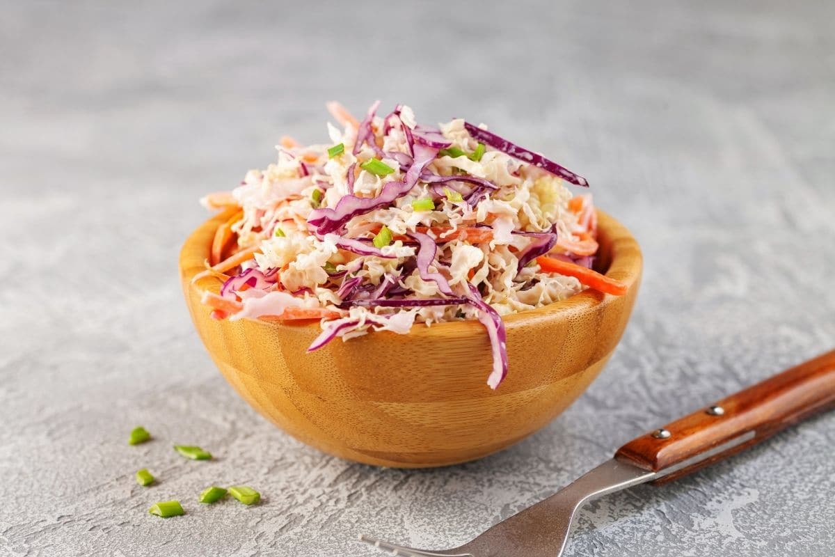 Wooden bowl of coleslaw salad next to fork on gray table