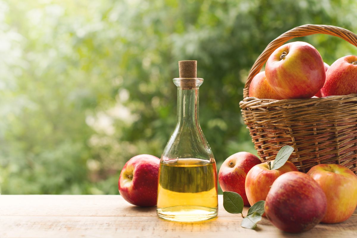 Bottle of apple cider next to fresh ripe apples.