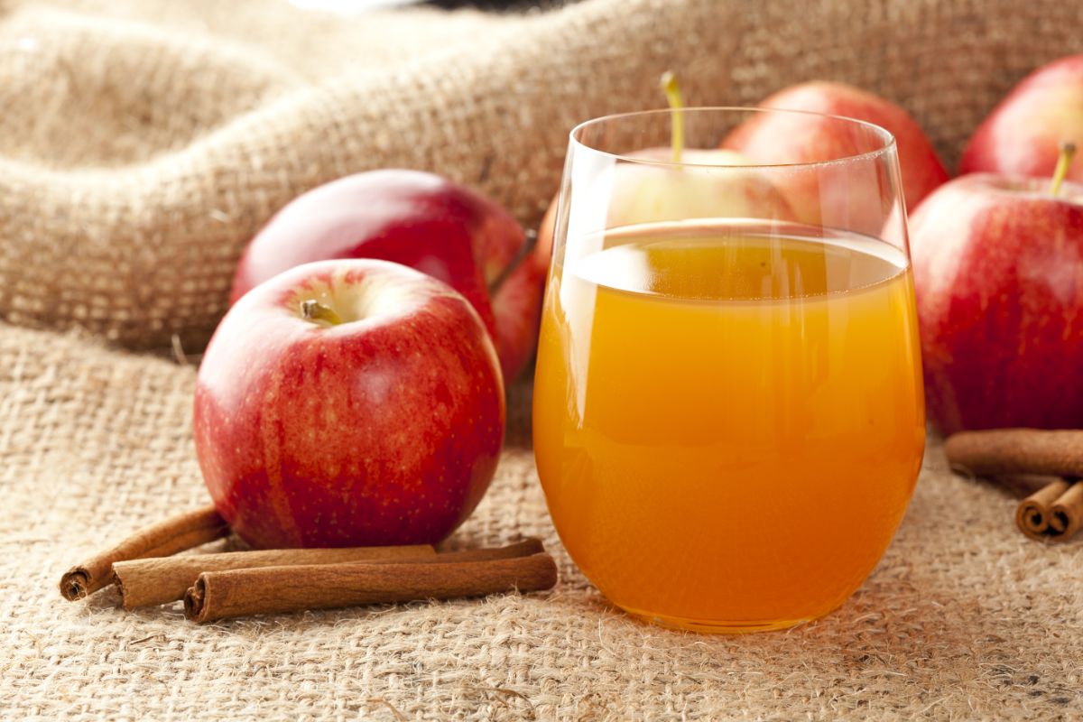 Glass of fresh apple cider with ripe apples around.