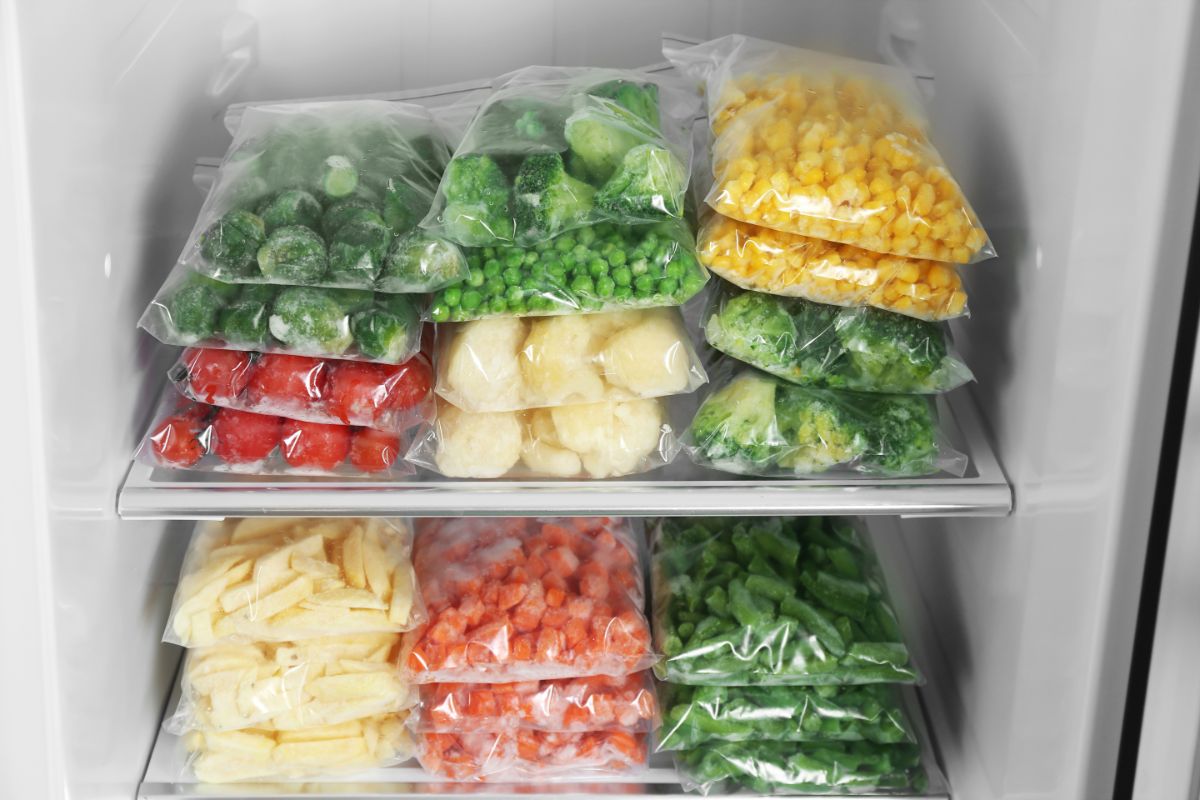 Bags of frozen vegetables stacked in a fridge.